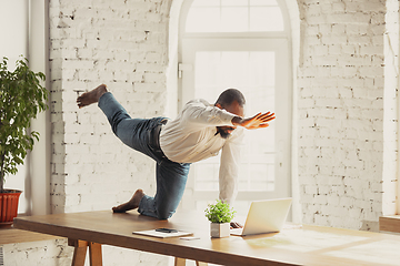 Image showing Young african-american man doing yoga at home while being quarantine and freelance working