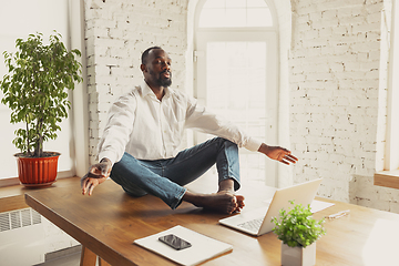 Image showing Young african-american man doing yoga at home while being quarantine and freelance working