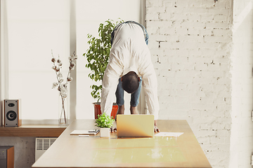 Image showing Young african-american man doing yoga at home while being quarantine and freelance working