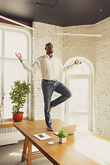 Image showing Young african-american man doing yoga at home while being quarantine and freelance working