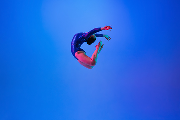 Image showing Young flexible girl isolated on blue studio background. Young female model practicing artistic gymnastics. Exercises for flexibility, balance.