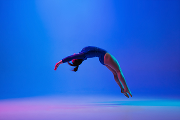 Image showing Young flexible girl isolated on blue studio background. Young female model practicing artistic gymnastics. Exercises for flexibility, balance.