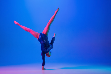 Image showing Young flexible girl isolated on blue studio background. Young female model practicing artistic gymnastics. Exercises for flexibility, balance.