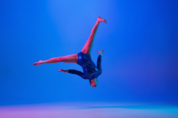 Image showing Young flexible girl isolated on blue studio background. Young female model practicing artistic gymnastics. Exercises for flexibility, balance.