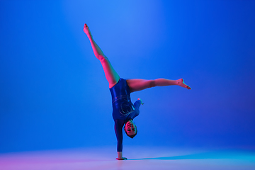 Image showing Young flexible girl isolated on blue studio background. Young female model practicing artistic gymnastics. Exercises for flexibility, balance.