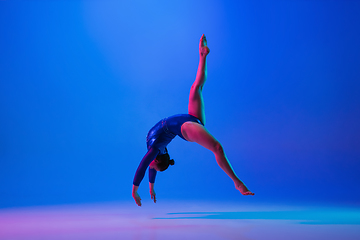 Image showing Young flexible girl isolated on blue studio background. Young female model practicing artistic gymnastics. Exercises for flexibility, balance.