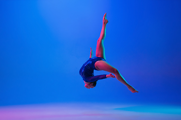 Image showing Young flexible girl isolated on blue studio background. Young female model practicing artistic gymnastics. Exercises for flexibility, balance.