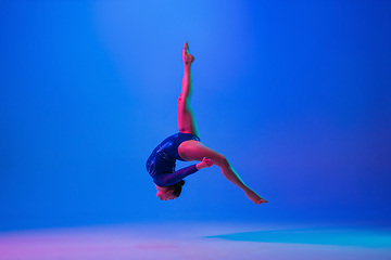 Image showing Young flexible girl isolated on blue studio background. Young female model practicing artistic gymnastics. Exercises for flexibility, balance.