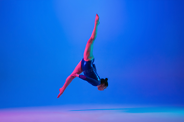 Image showing Young flexible girl isolated on blue studio background. Young female model practicing artistic gymnastics. Exercises for flexibility, balance.