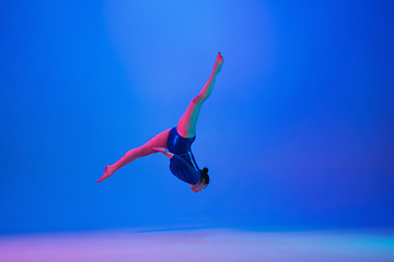 Image showing Young flexible girl isolated on blue studio background. Young female model practicing artistic gymnastics. Exercises for flexibility, balance.