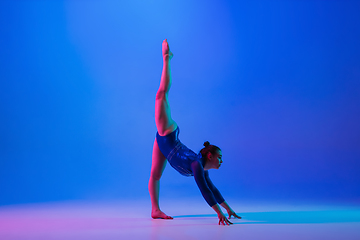 Image showing Young flexible girl isolated on blue studio background. Young female model practicing artistic gymnastics. Exercises for flexibility, balance.