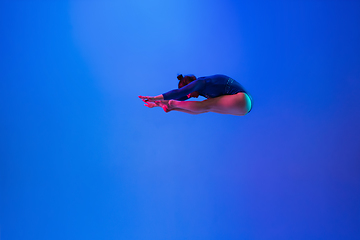 Image showing Young flexible girl isolated on blue studio background. Young female model practicing artistic gymnastics. Exercises for flexibility, balance.