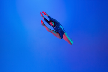 Image showing Young flexible girl isolated on blue studio background. Young female model practicing artistic gymnastics. Exercises for flexibility, balance.