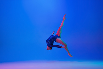 Image showing Young flexible girl isolated on blue studio background. Young female model practicing artistic gymnastics. Exercises for flexibility, balance.