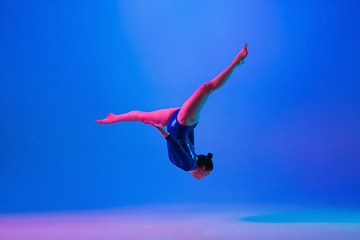 Image showing Young flexible girl isolated on blue studio background. Young female model practicing artistic gymnastics. Exercises for flexibility, balance.