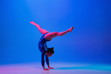 Image showing Young flexible girl isolated on blue studio background. Young female model practicing artistic gymnastics. Exercises for flexibility, balance.