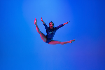 Image showing Young flexible girl isolated on blue studio background. Young female model practicing artistic gymnastics. Exercises for flexibility, balance.