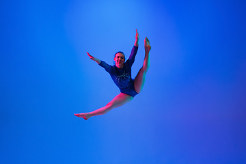 Image showing Young flexible girl isolated on blue studio background. Young female model practicing artistic gymnastics. Exercises for flexibility, balance.