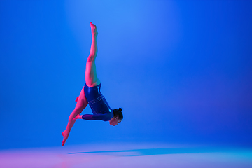 Image showing Young flexible girl isolated on blue studio background. Young female model practicing artistic gymnastics. Exercises for flexibility, balance.