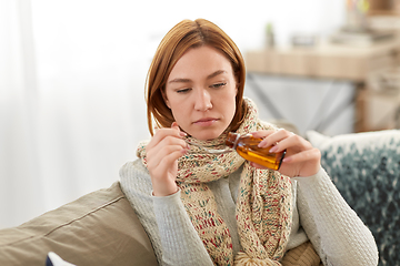 Image showing sick woman in scarf pouring cough syrup at home