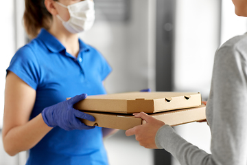 Image showing delivery girl in mask giving pizza boxes to woman