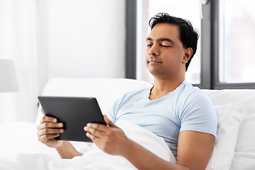 Image showing happy indian man with tablet pc in bed at home