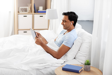 Image showing happy indian man with tablet pc in bed at home