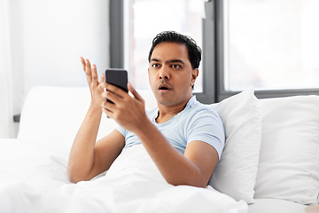 Image showing angry indian man with smartphone in bed at home