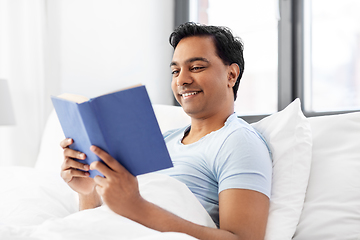 Image showing happy indian man reading book in bed at home
