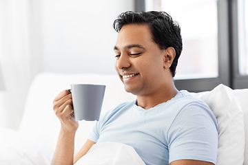 Image showing happy indian man drinking coffee in bed at home