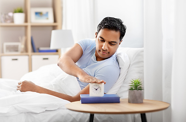 Image showing happy indian man with alarm clock lying in bed