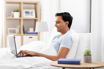 Image showing happy indian man with laptop in bed at home