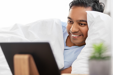 Image showing happy indian man with tablet pc in bed at home