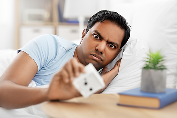 Image showing overslept indian man in bed looking at alarm clock