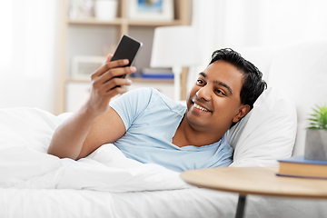 Image showing happy indian man with smartphone in bed at home