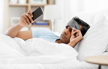 Image showing sleepy indian man with smartphone lying in bed