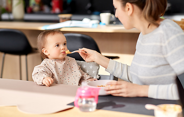 Image showing happy mother feeding baby with puree at home