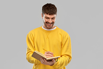 Image showing smiling man in yellow sweatshirt writing to diary