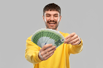 Image showing smiling young man in yellow sweatshirt with money