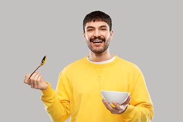 Image showing smiling young man with spoon and bowl eating