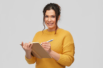 Image showing happy young woman writing to diary or notebook