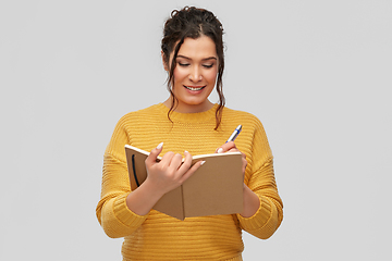 Image showing happy young woman writing to diary or notebook