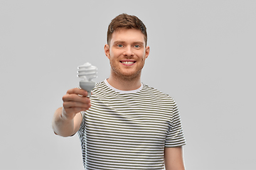 Image showing smiling young man holding lighting bulb