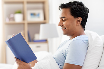 Image showing happy indian man reading book in bed at home