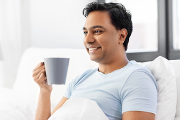 Image showing happy indian man drinking coffee in bed at home