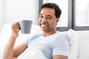 Image showing happy indian man drinking coffee in bed at home