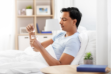 Image showing man in bed dropping medicine into glass of water