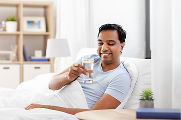 Image showing happy indian man drinking water lying in bed