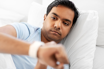 Image showing indian man looking at smart watch in bed at home