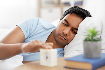 Image showing indian man with alarm clock lying in bed